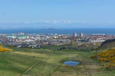 Holyrood Parkı 'ndan şehir merkezindeki Edinburgh şehrine genel hava manzarası, arka planda binalar ve deniz