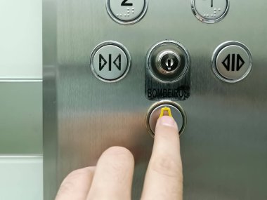 View of hand pressing emergency button on interior panel of an elevator