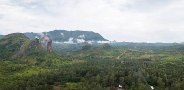 Orman ve dağlarla dolu tropikal bir arazinin hava fotoğrafçılığı, Kumbira Ormanı rezervi, muazzam jeolojik kaya elementleri, arka plan olarak bulutlu gökyüzü, Conda, Sumbe, Angola