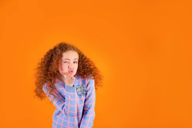 Turuncu arka planda kızıl saçlı, kıvırcık saçlı bir kız öpüşüyor.