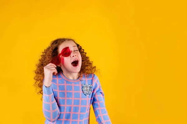 Kızıl saçlı, duygusal, sarı arka planda kırmızı gözlüklü bir kız.