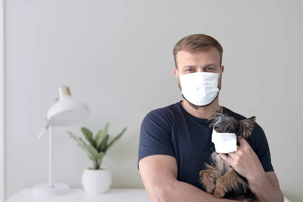 Portrait of caucasian young man holding a yorkshire terrier in a house environment both wearing face masks. Concept of coronavirus lockdown with pets