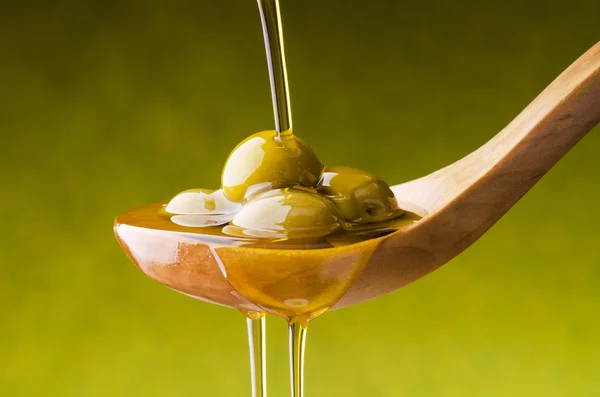 Una cuchara de madera con aceitunas verdes bajo la caída del aceite exstraver — Foto de Stock