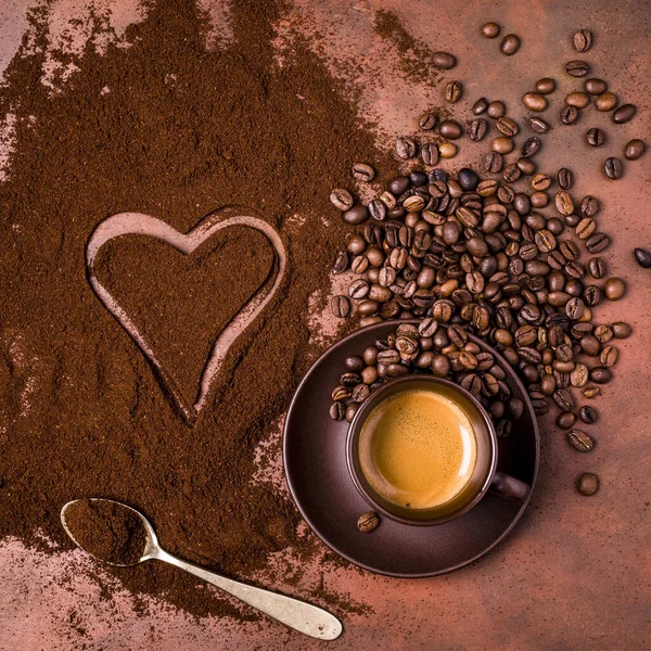 a cup of creamy espresso, a pile of ground coffee with a drawing of a heart