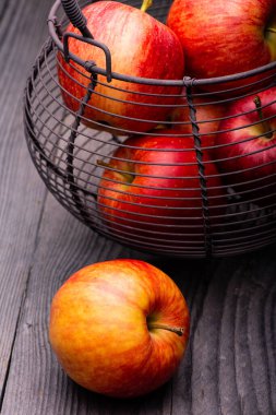 Sert ahşap masada, içinde elmalar olan metal bir sepet.
