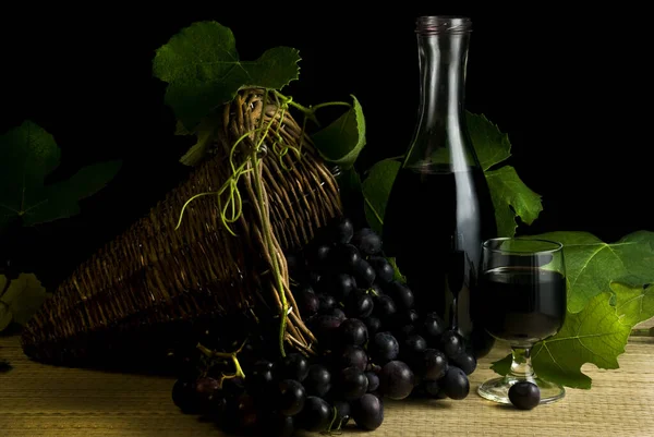 wicker basket with black grapes, a bottle and a glass of red wine