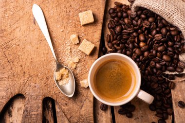Kırsal ahşap masada, ön planda, bir fincan espresso kahve, esmer şeker ve kızarmış kahve çekirdekleri..