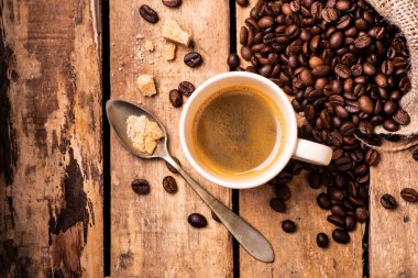 Kırsal ahşap masada, ön planda, bir fincan espresso kahve, esmer şeker ve kızarmış kahve çekirdekleri..