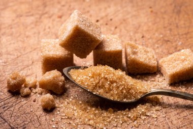 Ön planda, kaşıkta ham şeker kristalleri var. Arka planda biraz küp şeker var.