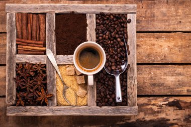 Kırsal ahşap masada, üst manzaralı, bir fincan espresso, çeşitli baharatlarla dolu ahşap bir kap, çiğ şeker ve kahve çekirdeği.