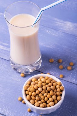 Masanın üzerinde açık mavi odunlar, sarı soya fasulyesi ve soya sütü ön plandaki bardakta.