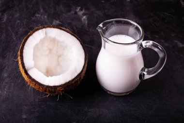 Ön manzara, yarım hindistan cevizi ve hindistan cevizi sütü cam sürahide, koyu arkaplanda.