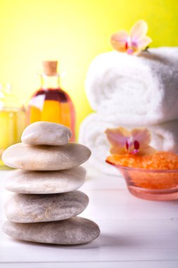 Ön planda istiflenmiş taşlar, arka planda beyaz havlular, orkideler, aromatik banyo tuzları, birkaç mum ve parfüm esanslı şeffaf şişeler var..