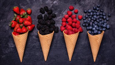 Ön planda yüksek açılı manzara, kırsal ve koyu arka planda, dondurma külahlarında taze böğürtlen çeşitliliği.