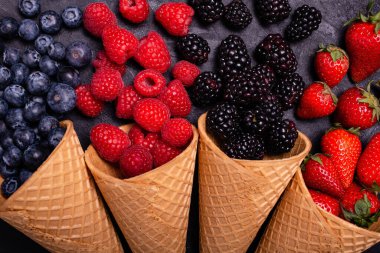 Ön planda yüksek açılı manzara, kırsal ve koyu arka planda, dondurma külahlarında taze böğürtlen çeşitliliği.