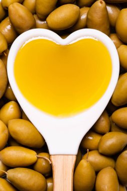 In the foreground, with a view from above, background with green olives and white spoon, heart-shaped, with extra virgin olive oil. clipart