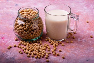 Kırsal bir arka planda, bir bardak soya sütü ve temiz cam kasede soya fasulyesi.