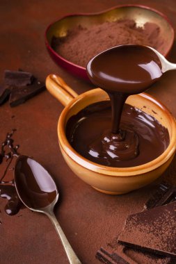 Kahverengi arka plan, kakao ve çikolata parçalarıyla kaplanmış, biraz çikolata ve erimiş siyah çikolatalı bir kase.