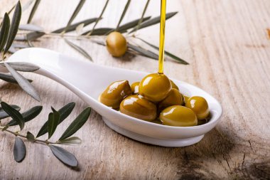 Ekstra bakire zeytinyağı kırsal ahşap masadaki yeşil zeytinlerle dolu seramik kaseye akar.