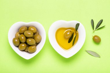 Üst manzara, yeşil arka planda, kalp şeklinde iki beyaz seramik kâse zeytinyağı ve ekstra saf zeytinyağı.