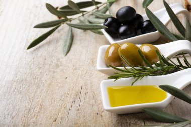 Ön planda, kırsal ahşap masada, yeşil ve siyah zeytinli beyaz seramik kaseler ve ekstra saf zeytinyağı..