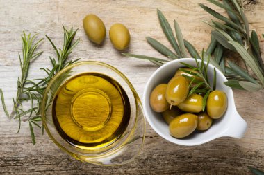 Üst manzara, ön planda, kırsal ahşap masada, zeytinli kaseler, biberiye ve ekstra saf zeytinyağı. Durgun hayat