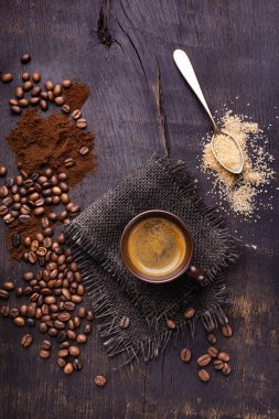 Çiğ ve koyu ahşap masada, bir fincan kahve, bir kaşık kahverengi şeker ve kavrulmuş kahve çekirdekleri..