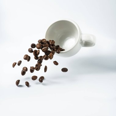 Beyaz arkaplandan izole edilmiş, bir fincan kahve havada asılı kalmış ve kahve çekirdekleri şelalesinden taşmış.