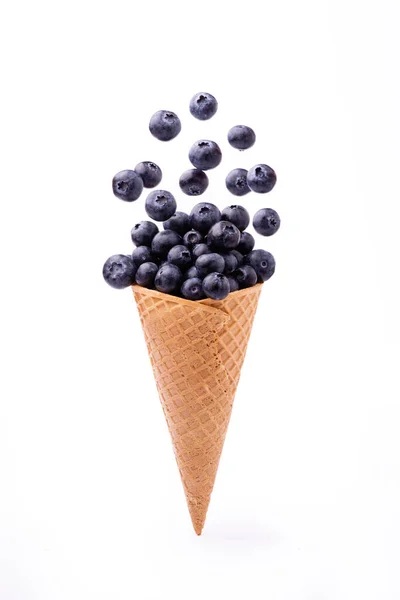 前景では 白い背景から隔離されたアイスクリームコーンの新鮮なブルーベリーのカスケード — ストック写真