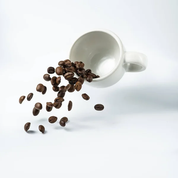 isolated from the white background, a cup of coffee suspended in the air from which a cascade of roasted coffee beans flows