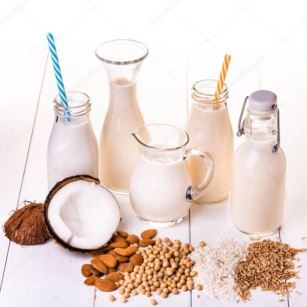 types of vegetable milk, and organic, in glass containers on the table in white wood