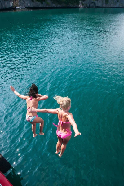 Две счастливые девушки в бикини прыгают с деревянной лодки . — стоковое фото