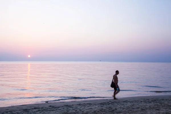 Hombre de pecho desnudo caminando por la playa al atardecer . — Foto de Stock