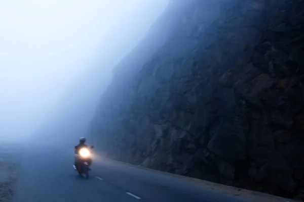 Viaggiatore maschile in sella alla moto sulla strada buia e nebbiosa . — Foto Stock