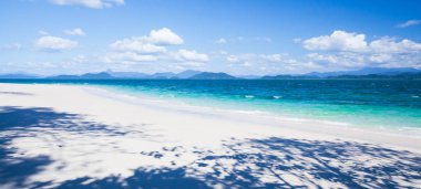 Yazın güneşli, güneşli, berrak ve güzel bir tropikal deniz manzarası. Beyaz kumlu plajlar ve mavi gökyüzüne karşı beyaz bulutlar. Saf kumsaldaki vahşi ağaçların muhteşem gölgeleri. Khang Khao Adası, Tayland.