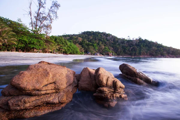 夕暮れ時の熱帯砂のビーチで茶色の石は 柔らかい夕日が大きな石の形に優しく波に輝き タイのラノン島のコチャン島での夏のシーン 長時間露光 — ストック写真