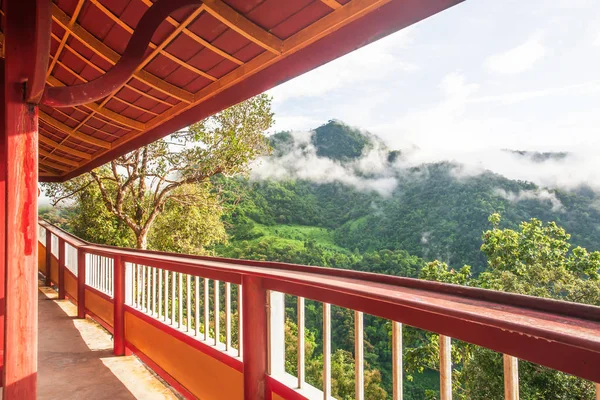 Tranquil mountains view from long iron balcony, picturesque of tropical mountain range in misty rainy, warm sunrise shines on the branches of wild trees.