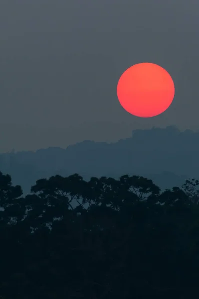 Fantastic the red sun setting above the deep jungle and mountain range, art shape of the sun and wild trees at dusk, dark spot on the sun, winter scene in Khao Yai National Park, Thailand.