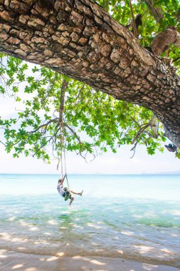 Mutlu çocuk yaz günü deniz kenarında salıncakta salıncakta oynuyor, mutlu çocuk deniz kenarında tropikal ağacın gölgesinde oynuyor. Koh Mook, Tayland.