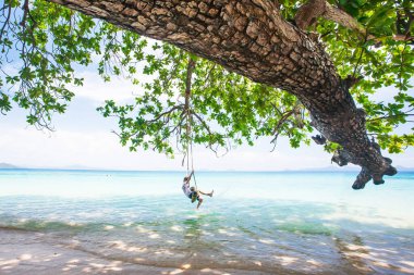 Mutlu çocuk yaz günü deniz kenarında salıncakta salıncakta oynuyor, mutlu çocuk deniz kenarında tropikal ağacın gölgesinde oynuyor. Koh Mook, Tayland.