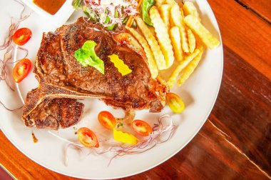 Orta pişmiş ızgara biftek, salata, patates kızartması, ahşap masada servis edilen taze domatesler. Düz yat, üst görünüm, kapat.