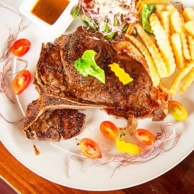 Orta pişmiş ızgara biftek, salata, patates kızartması, ahşap masada servis edilen taze domatesler. Düz yat, üst görünüm, kapat.