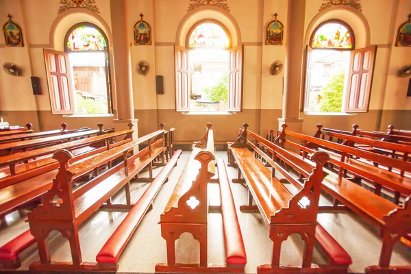 A tranquil the ancient church interior with old wooden church benches, glowing sunbeam shines through old windows and stained glass on old wooden church benches, Santa Cruz Church or Kudi Chin, Thailand.