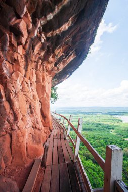 Kırmızı kumtaşı uçurumunun kenarındaki eski ahşap köprü tarla ve arka planda mavi gökyüzü. Bueng Kan, Tayland.