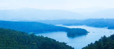 Mavi sisli bir dağ sırasındaki Sirikit Gölü 'nün resimli hava manzaralı manzarası. Mavi gölde sallı ağları olan yerel bir balıkçı. Nan, Tayland.
