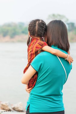 Annesinin kollarında küçük bir Asyalı kız, annesinin kollarında dikiz aynasından gün batımında bir nehir kıyısında dinlenirken..