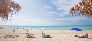 Bir grup turist, yaz günü plaj sandalyelerinde kitap okuyup rahatlıyor, Palmiye yapraklarının sahil barından dışarı bakıyor, güneşli arka planlarda pitoresk bir tropikal deniz görüyor. Khao Lak, Tayland.