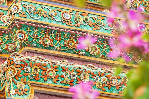 Elegant flower mosaic tiles of stupa of Wat Pho, Thailand. Wat Pho known also as the Temple of the Reclining Buddha. Pink flowers blurred on foreground. The temple is open to the public.