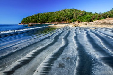 Güneşli yaz mevsiminde siyah kumlu bir plaj. Siyah kumsal dalgalarıyla tropikal adanın büyüleyici manzarası. Koh Chang, Tayland.