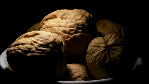 Nueces en un tazón blanco girando sobre fondo negro con luz cenital — Vídeos de Stock